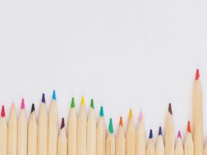 A row of vibrant colored pencils aligned on a white background, providing ample copyspace.