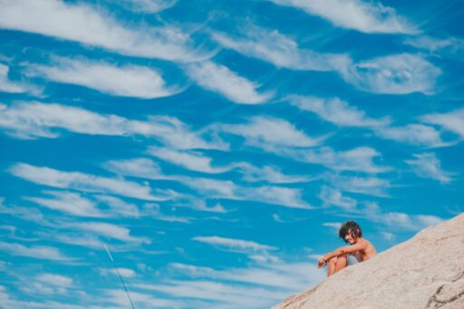 A man sitting on a beach under the sky, possibly thinking about taking a plunge into the sea. The huge expanse of sky and clouds stands for a large enterprise where you have to make a lot of considerations before starting marketing campaigns. Inexperienced marketers even more so.